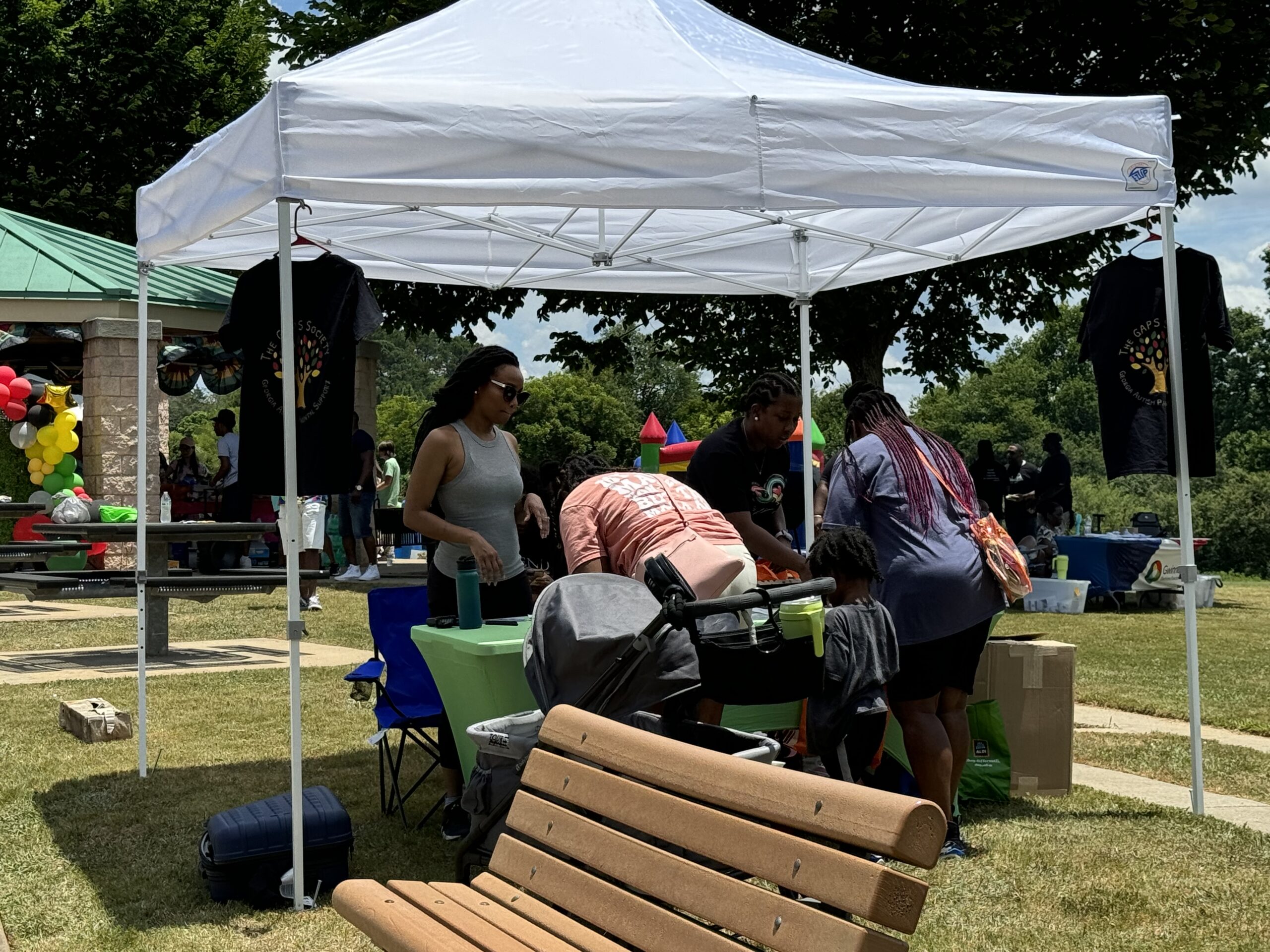 photo of two black women at a GAPS event booth filling out information, a young black boy standing between them, and two black women working the booth, everyone under a white tent