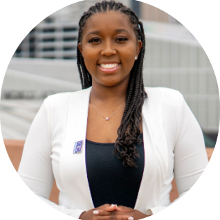 Shakuro Castro headshot, she has dark skin, long braids, and is wearing a white coat.