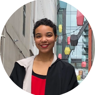 Keya Gibbons headshot. They have light brown skin and a curly pixie haircut, and they're wearing a red shirt with a black jacket